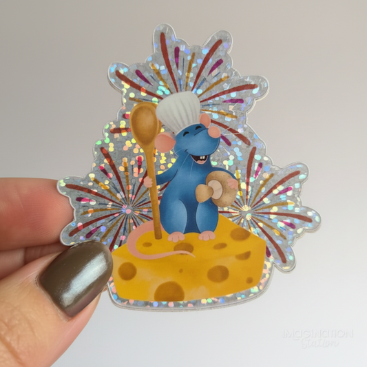 Holographic sticker of a cartoon mouse holding a wooden spoon on a cheese block with fireworks in the background.