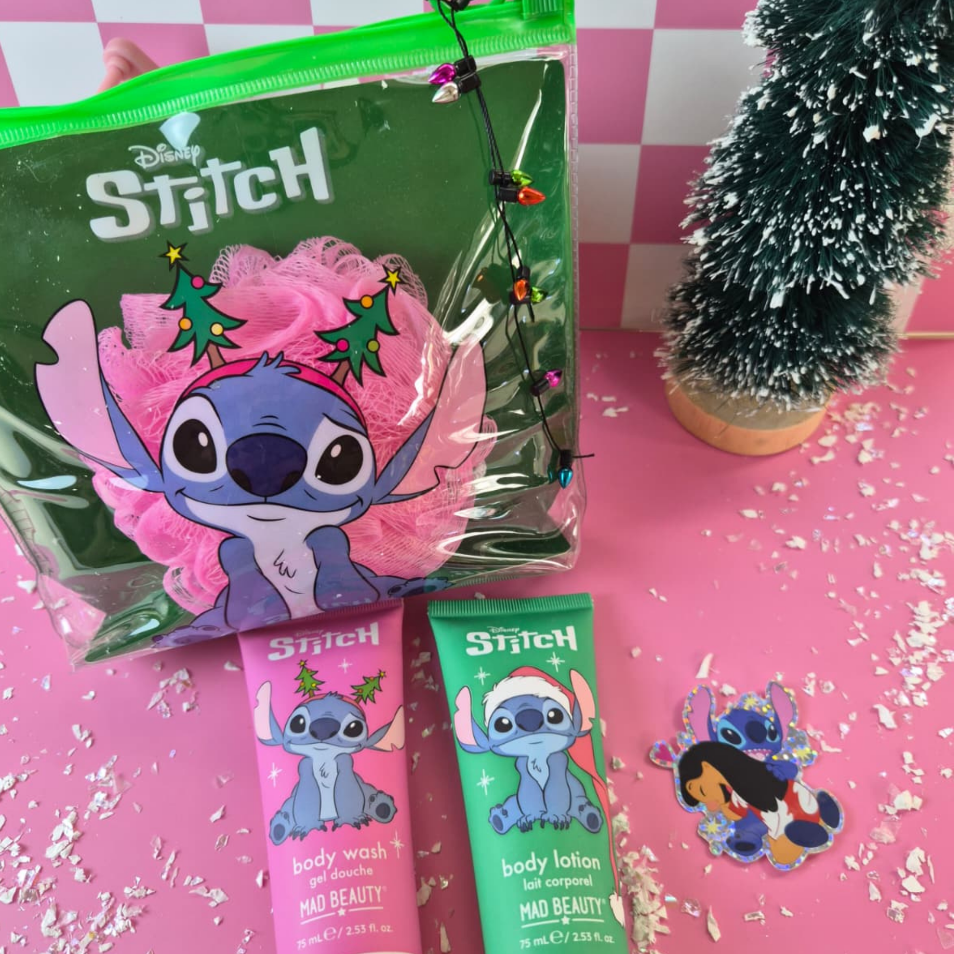 Disney Stitch themed products including a bag, body wash, and lotion on a pink checkered background with a small Christmas tree.