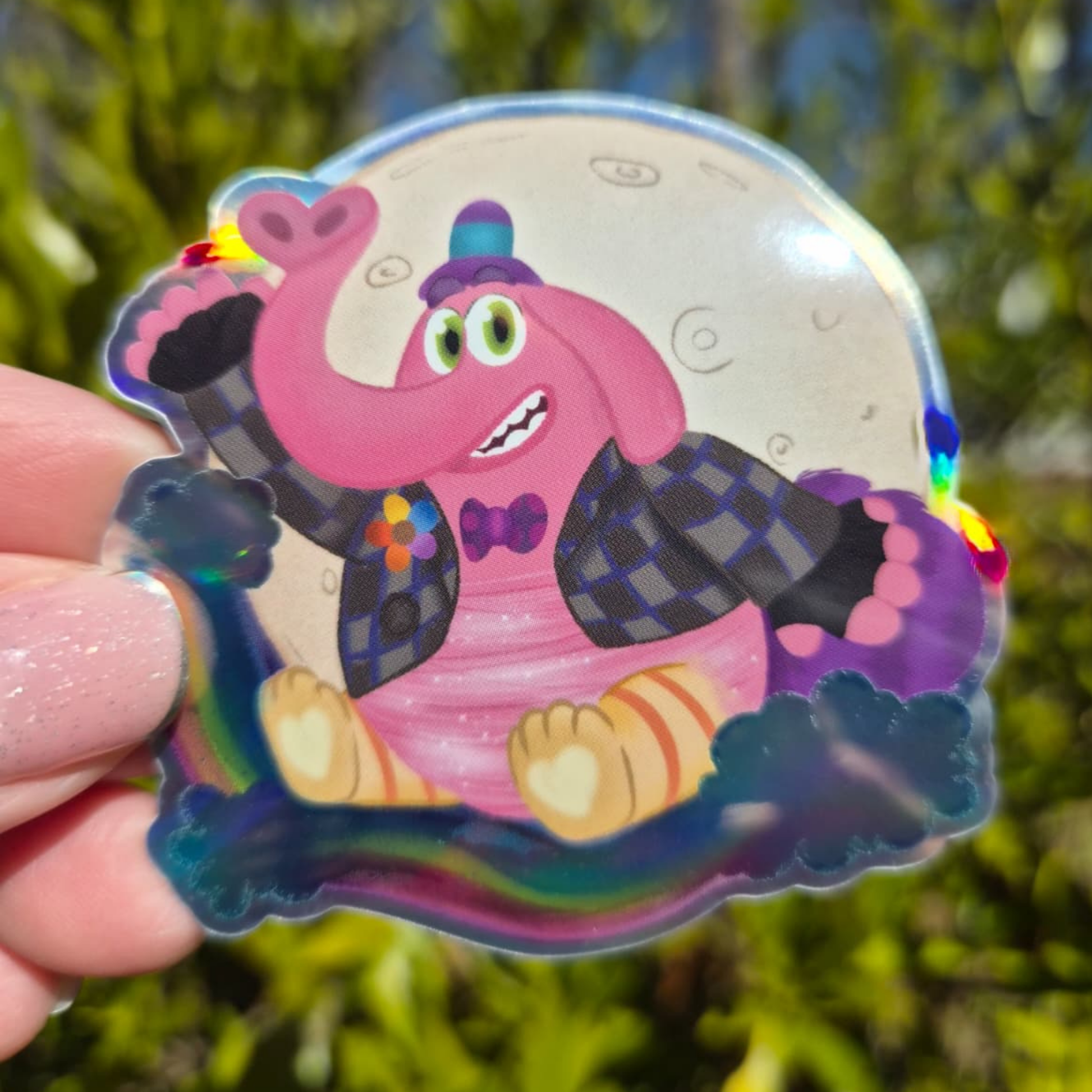 Colorful cartoon character sticker held in front of a blurred natural background