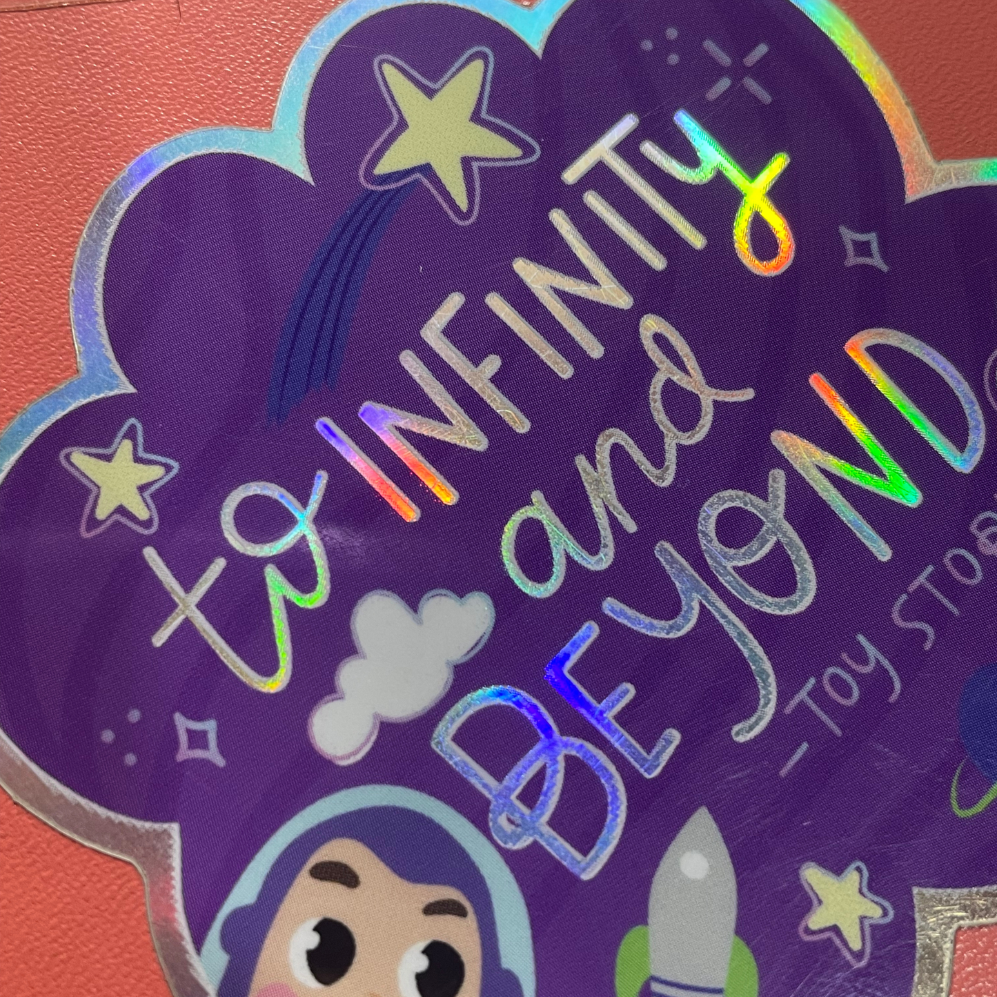 Holographic 'To Infinity and Beyond' sticker with cartoon character on a purple background